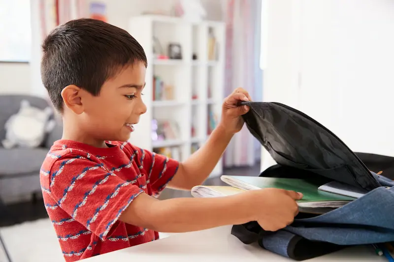 Young boy packing his backpack for school.
