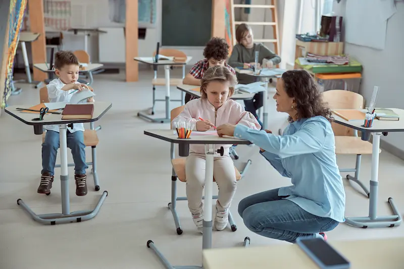 A female teacher is helping elementary students in a classroom.