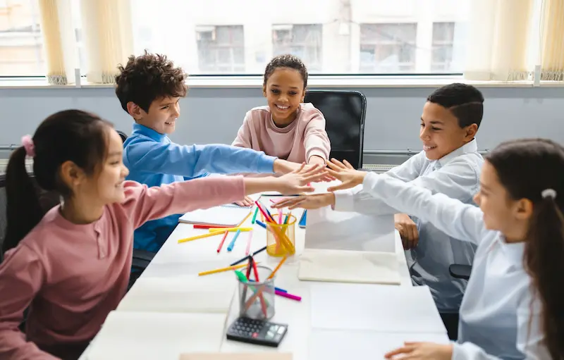 Enthusiastic children putting their hands together to collaborate on a group project.