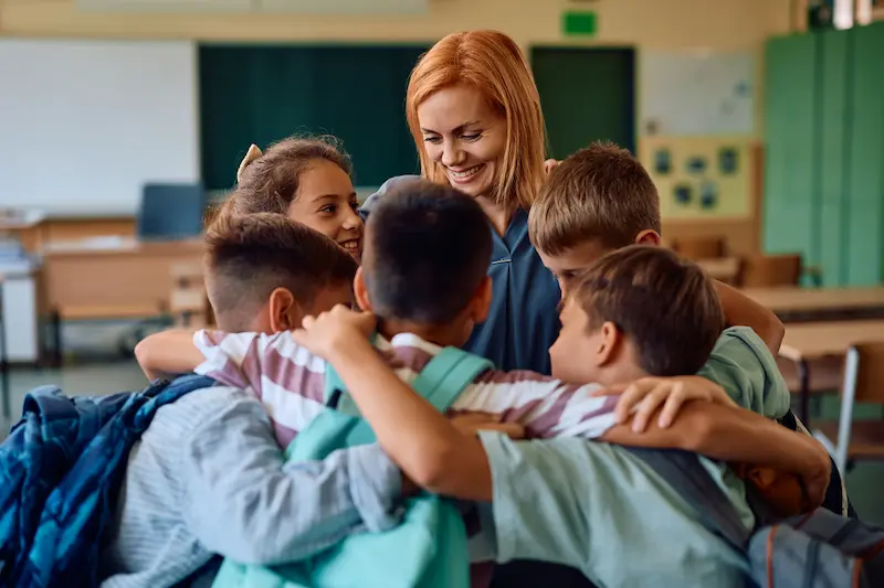 Teacher hugging a group of her students in a classroom.