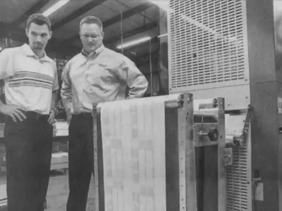 Photo from a newspaper article of two employees watching a datebook being printed.