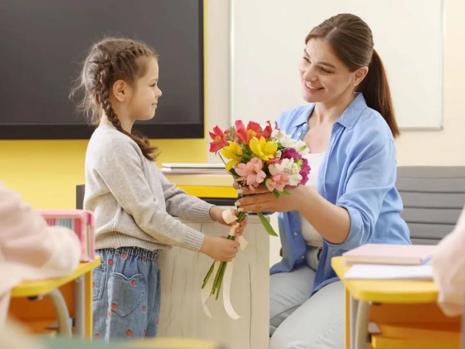 Young girl handing a colorful bouquet of flowers to her teacher.
