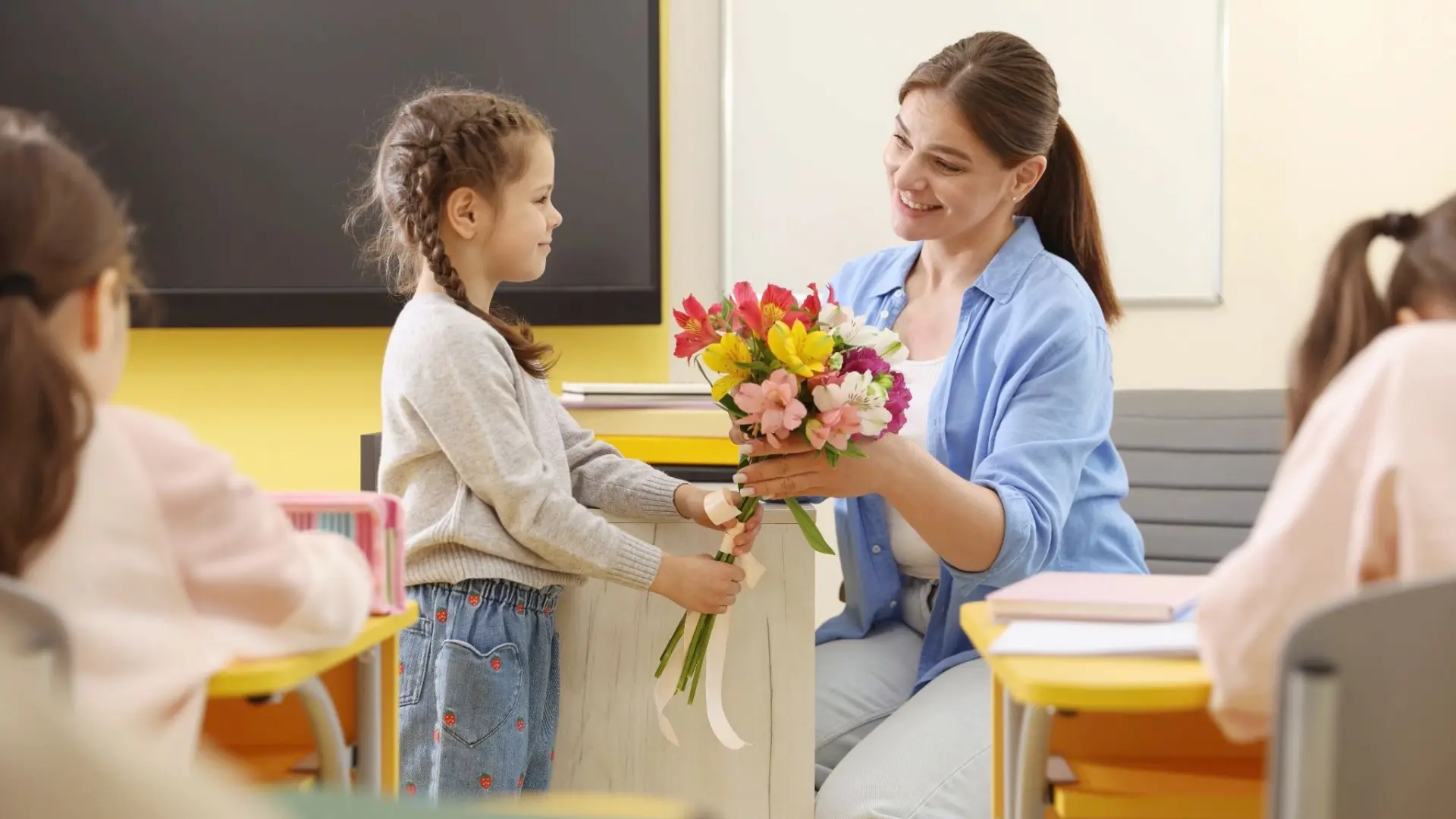 Young girl handing a colorful bouquet of flowers to her teacher.
