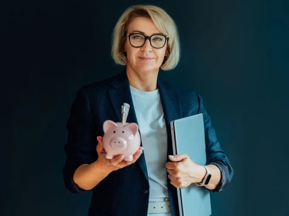 Adult woman holding a piggy bank and a laptop.