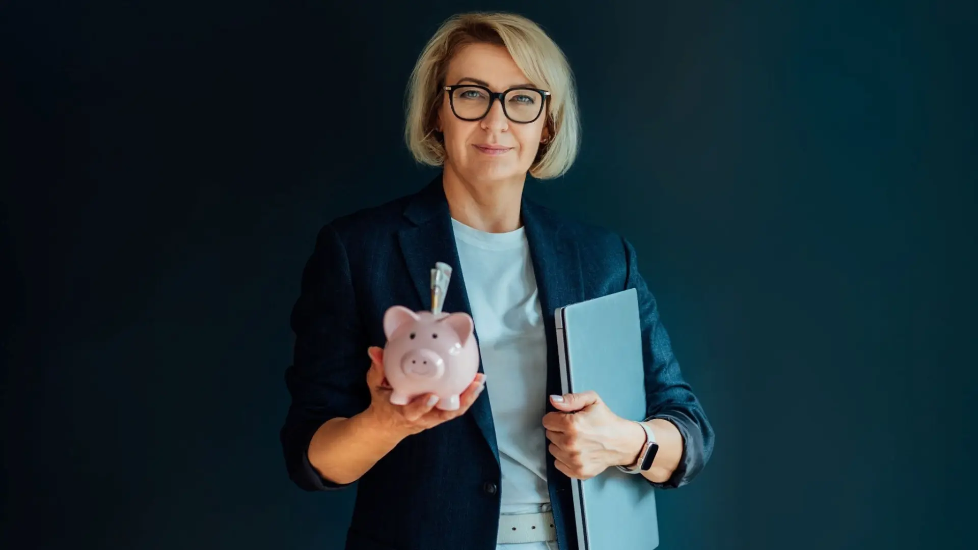 Adult woman holding a piggy bank and a laptop.